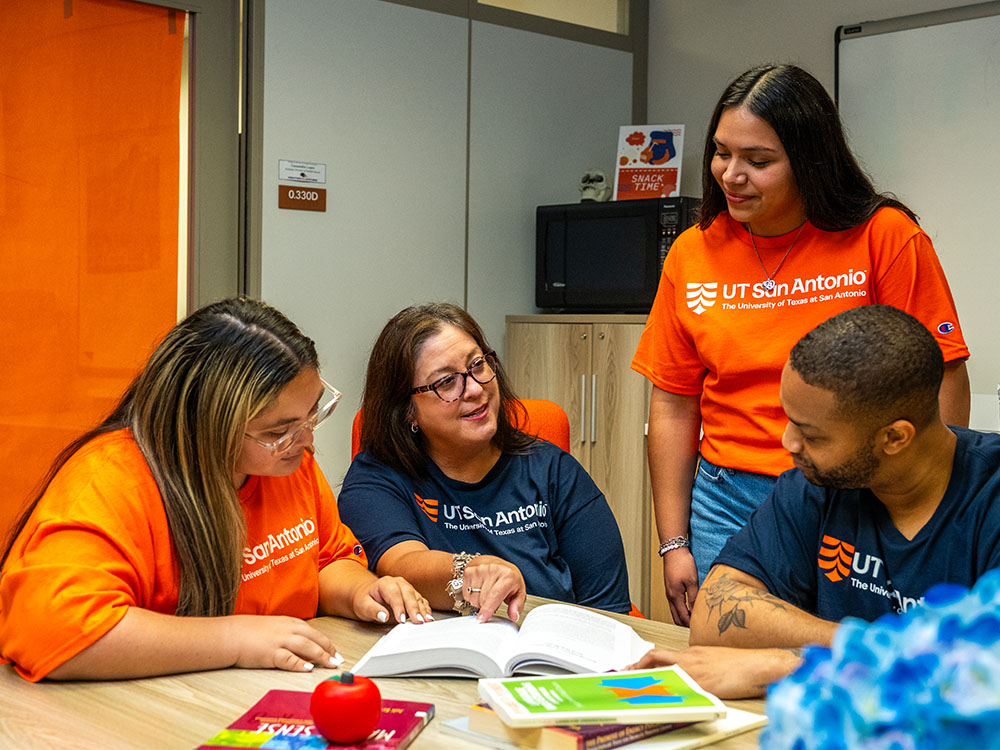 College of Education and Human Development students at a table with a faculty member learning from a textbook