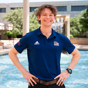 Conrad Finos BBA Cyber Security graduate in front of UTSA fountain