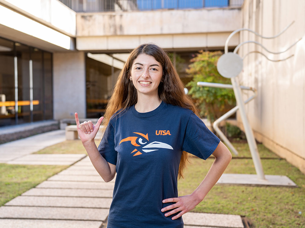 UTSA student with Birds Up in a green courtyard.