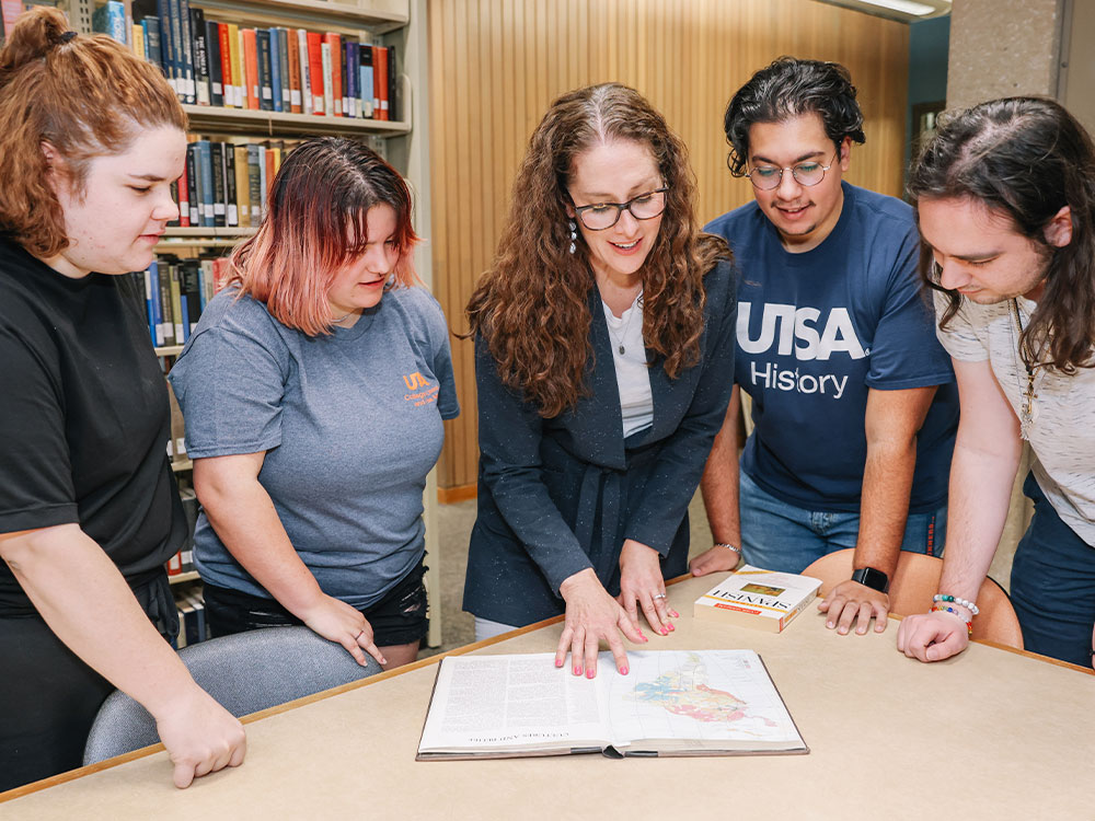 UTSA professor and students examining a textbook.