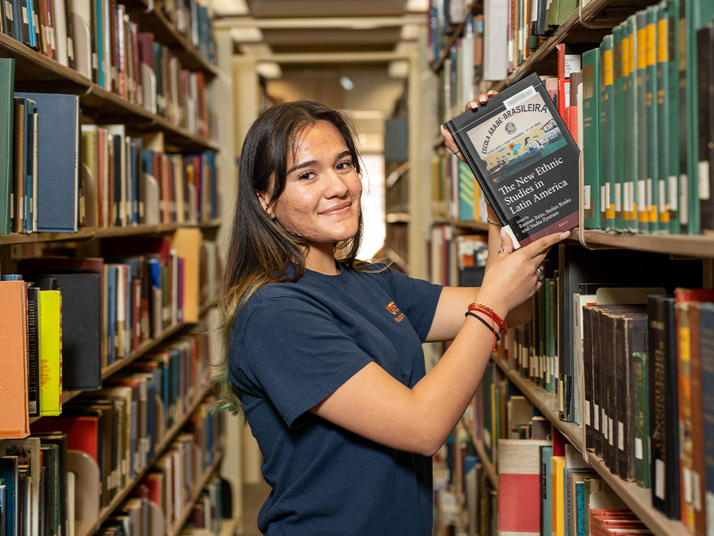 Student in library taking book off shelf