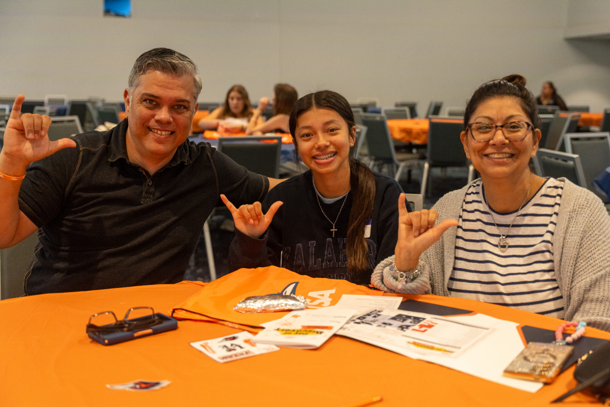 Two adults and a child sit together giving the UTSA 'Birds Up' hand sign.
