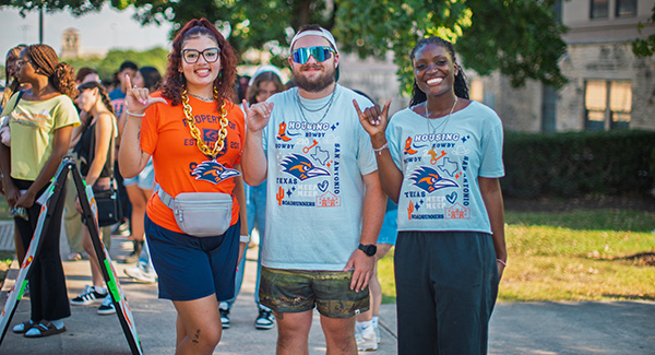 Three students at the housing block party on campus giving the birds up hand sign