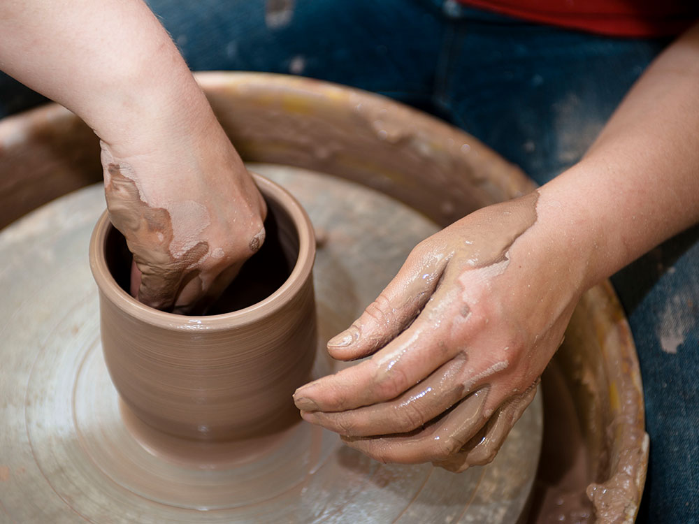 A pair of hands molding clay on a pottery wheel.