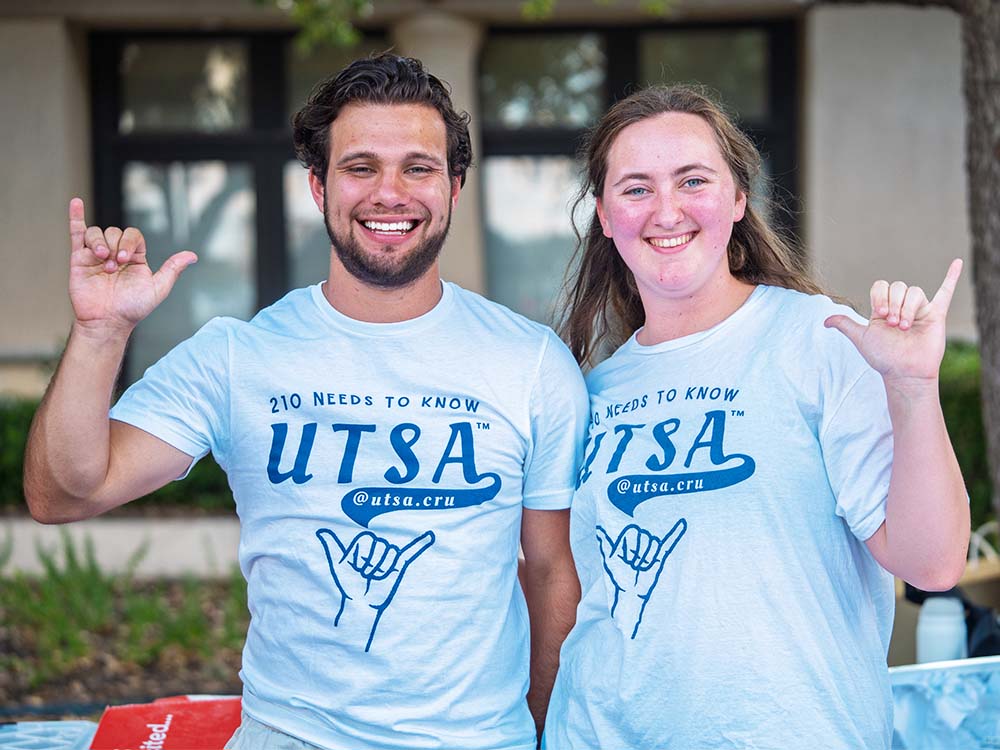 Two students giving the birds up hand sign outside