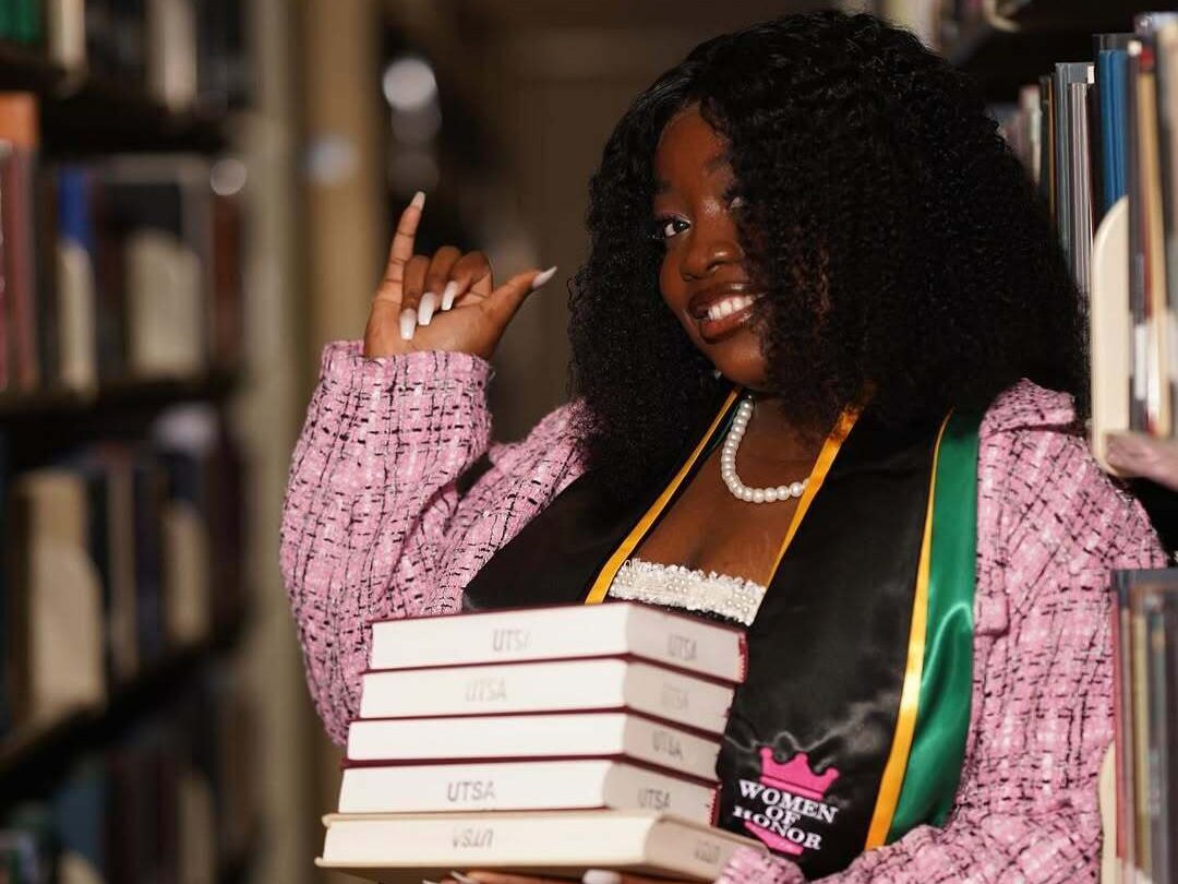 Ene John-Mark holding a stack of books in a library.