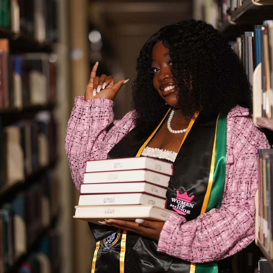 Ene John-Mark holding a stack of books in a library.