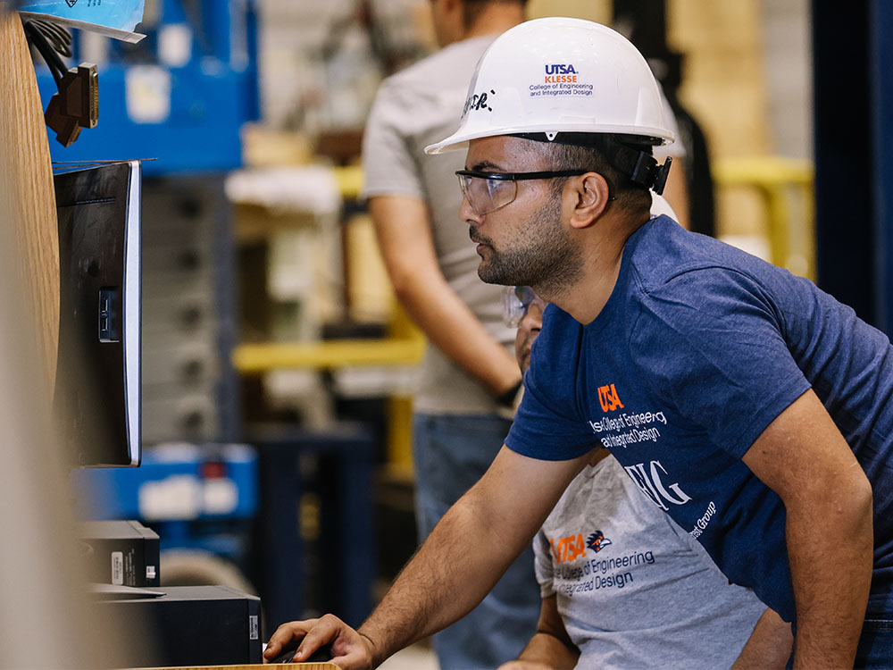 UTSA student in hard hat using computer in construction area